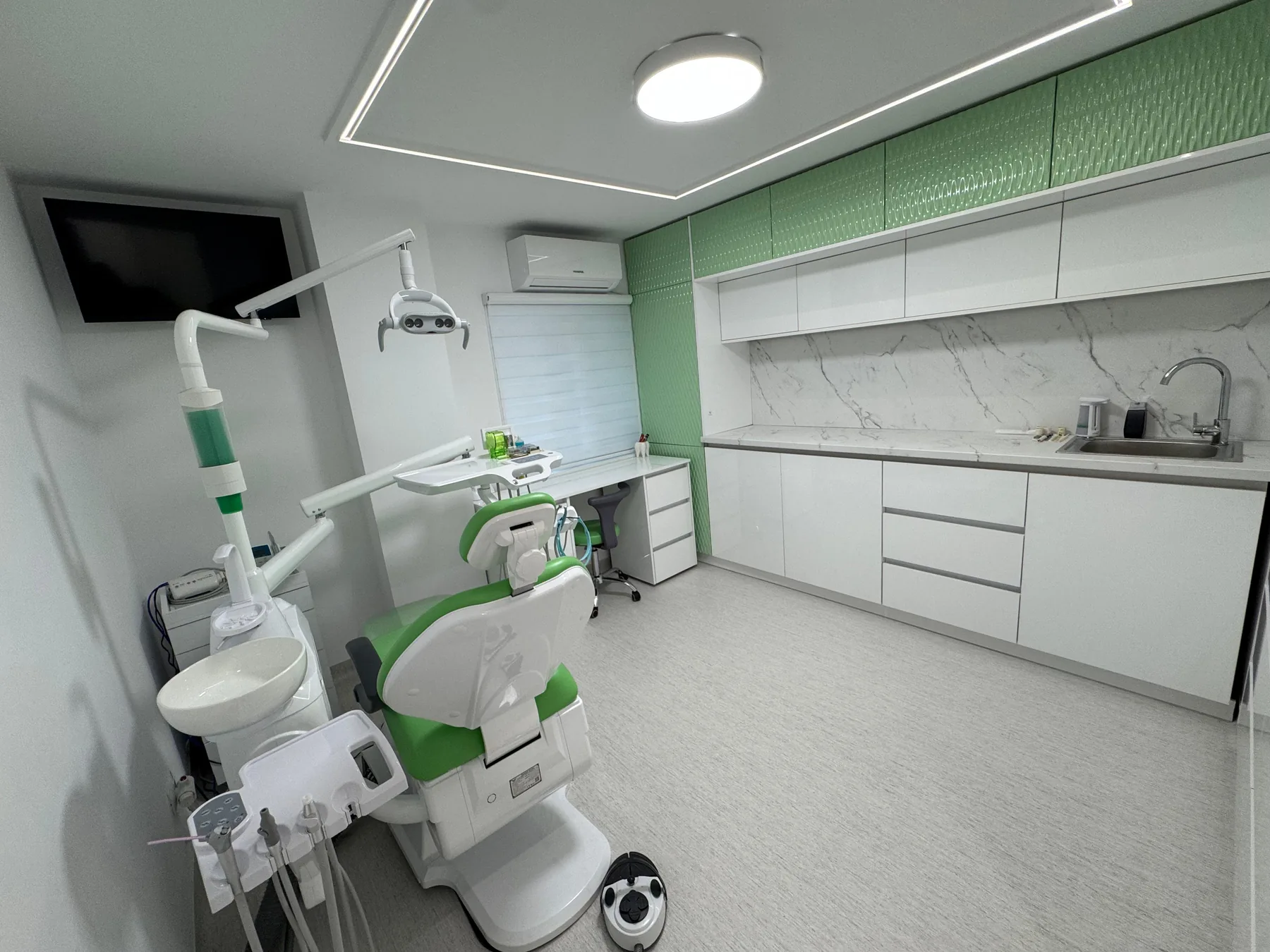 Fotoliul stomatologic verde, într-un cabinet luminos cu mobilier alb și marmură